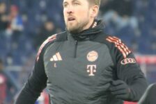 Harry Kane wearing a black Bayern Munich training jacket before a match, with the club badge visible on his chest.