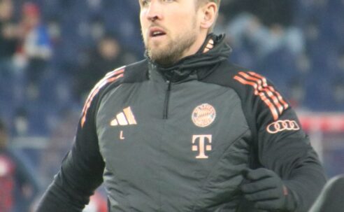 Harry Kane wearing a black Bayern Munich training jacket before a match, with the club badge visible on his chest.
