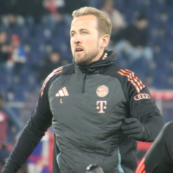 Harry Kane wearing a black Bayern Munich training jacket before a match, with the club badge visible on his chest.
