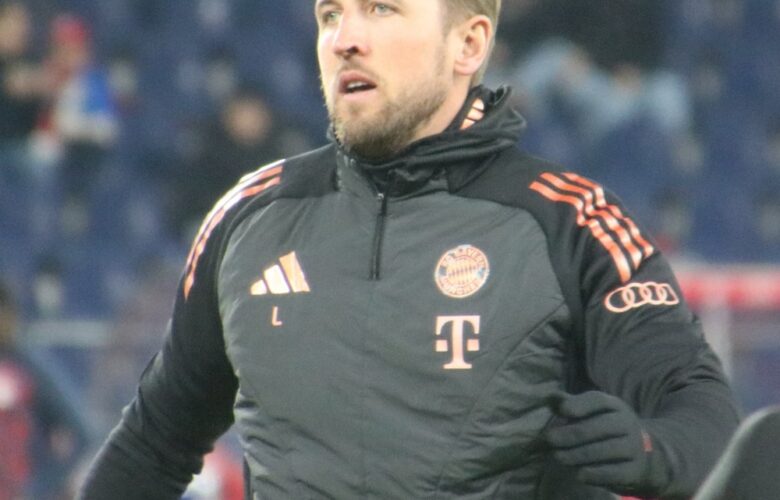 Harry Kane wearing a black Bayern Munich training jacket before a match, with the club badge visible on his chest.